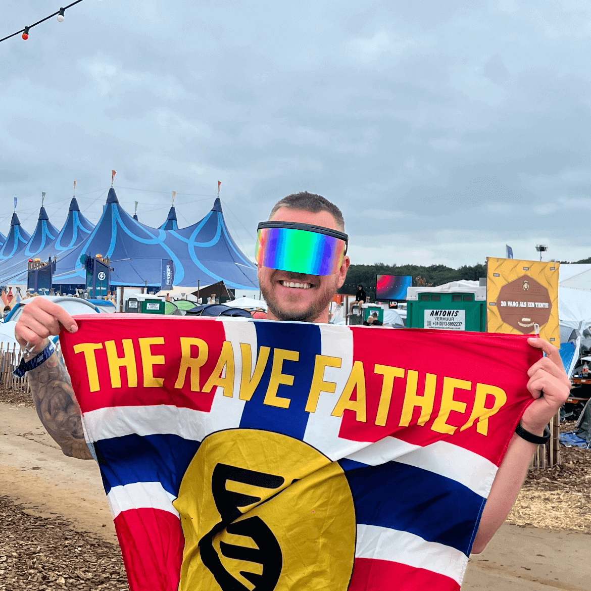 Man wearing RaveFather Oversized Rave Visor holding a flag with "The Rave Father" text at an outdoor festival