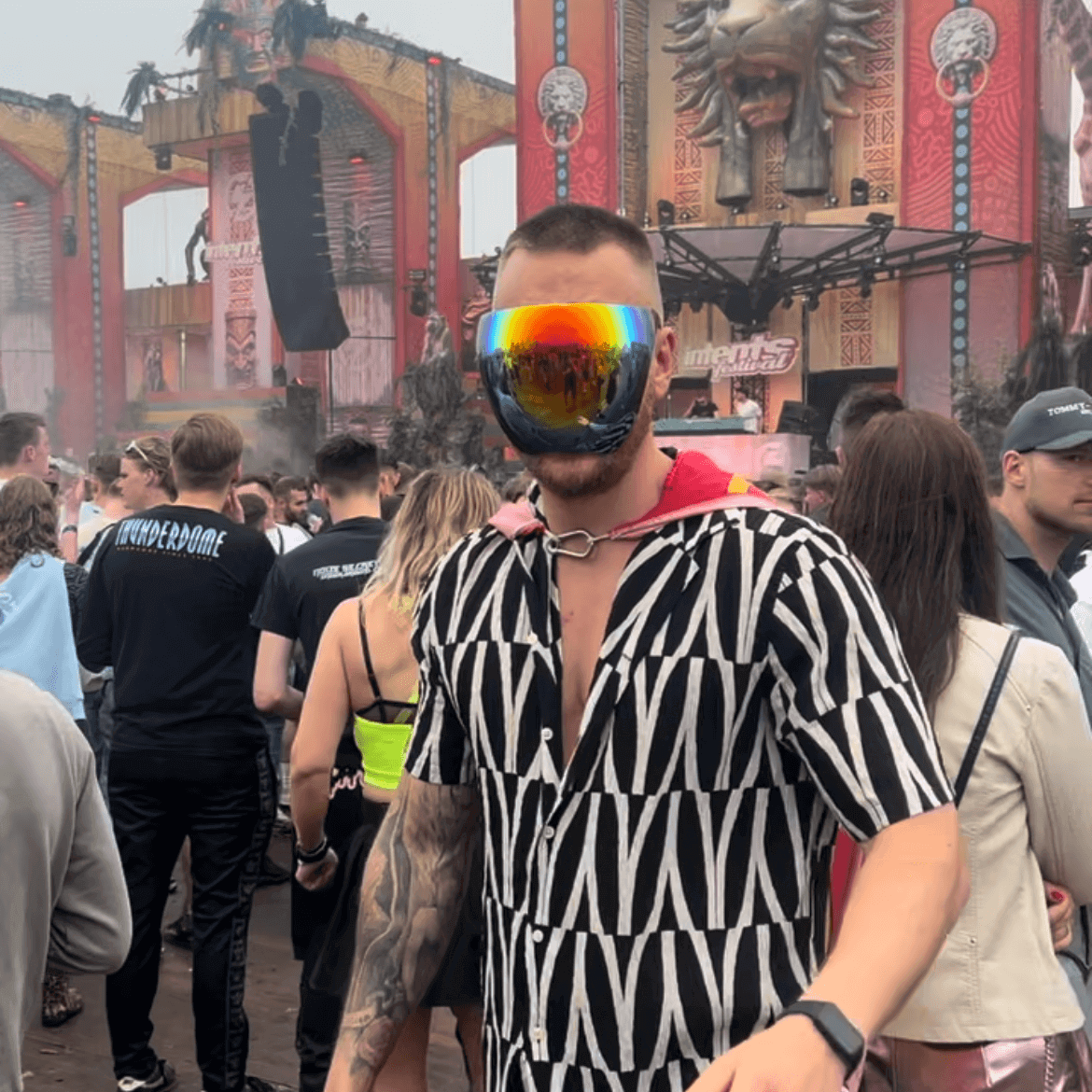 Man wearing RaveFather Rave Mask at a vibrant festival with colorful stage background